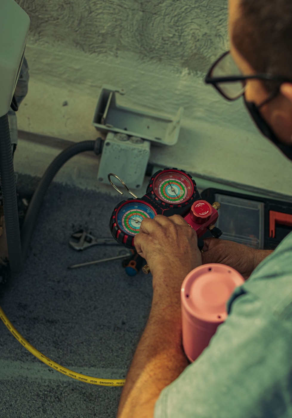 A technician reading refrigerant pressures on a manifold gauge beside an outdoor AC unit